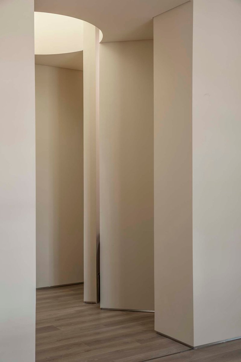 View through curving white partitions creating layered openings with pale wood flooring