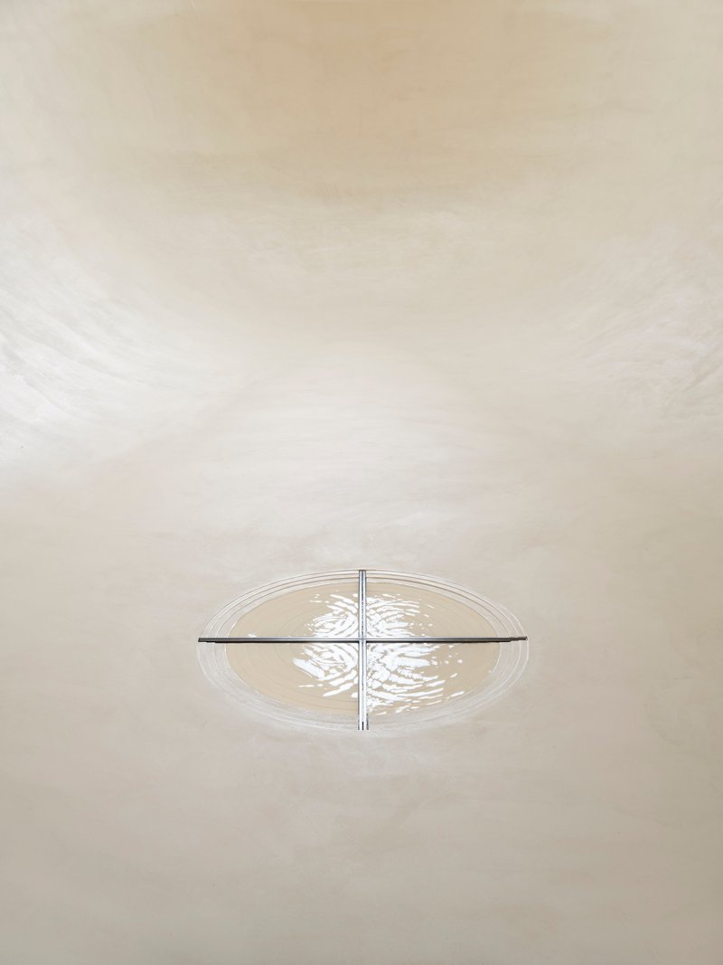 Overhead view of cruciform light fixture casting patterned shadows on curved white plaster vault