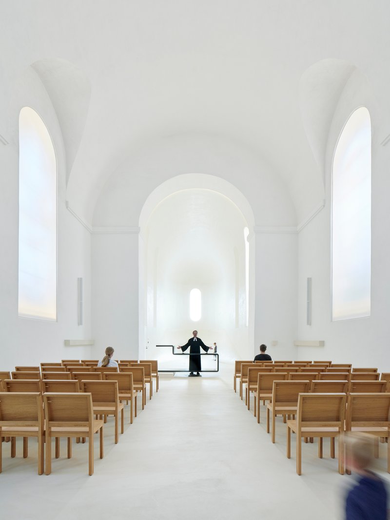 Whitewashed nave with barrel-vaulted ceiling, timber pews, and arched windows flooding the space with daylight