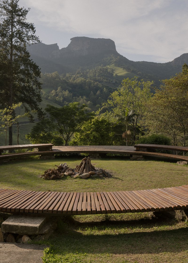 Circular timber deck platforms on grass with a central fire pit overlooking forested mountains