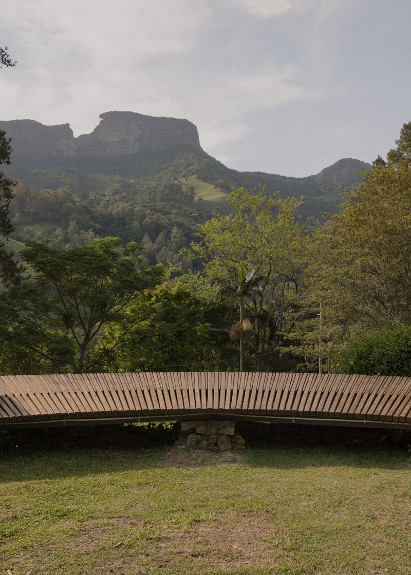 Horizontal slatted timber bridge spanning grass with mountain cliffs rising behind in mist