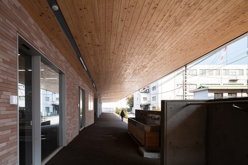 Covered walkway with timber plank ceiling, brick wall, and a person walking toward sunlight