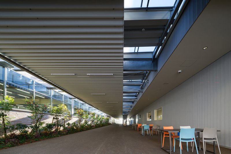 Covered outdoor corridor with skylights, planted beds, and colorful seating along a textured concrete floor