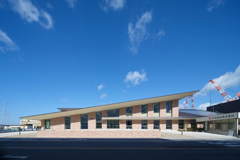 Street view of the horizontally banded brick facade with a cantilevered roof and construction cranes in the background