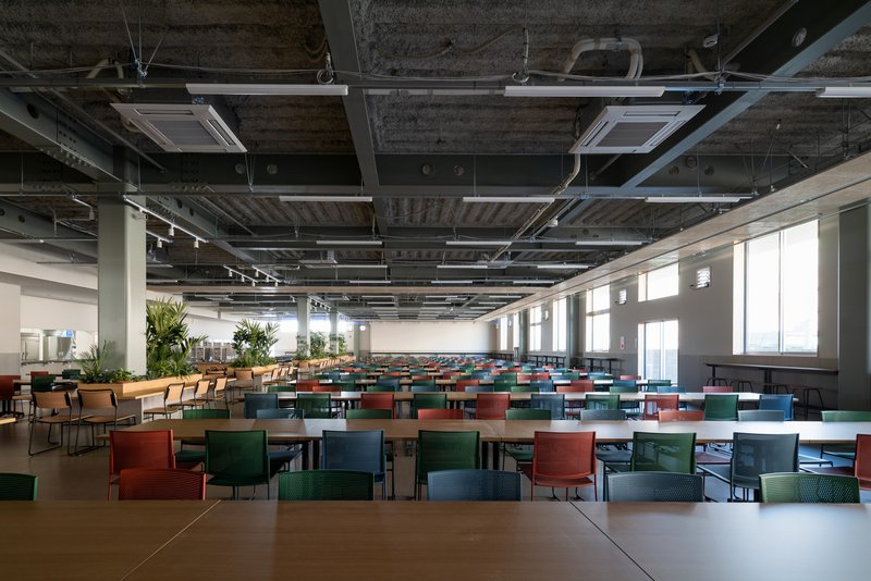 Cafeteria with multicolored seating arranged in rows under an exposed concrete ceiling with cassette air conditioners