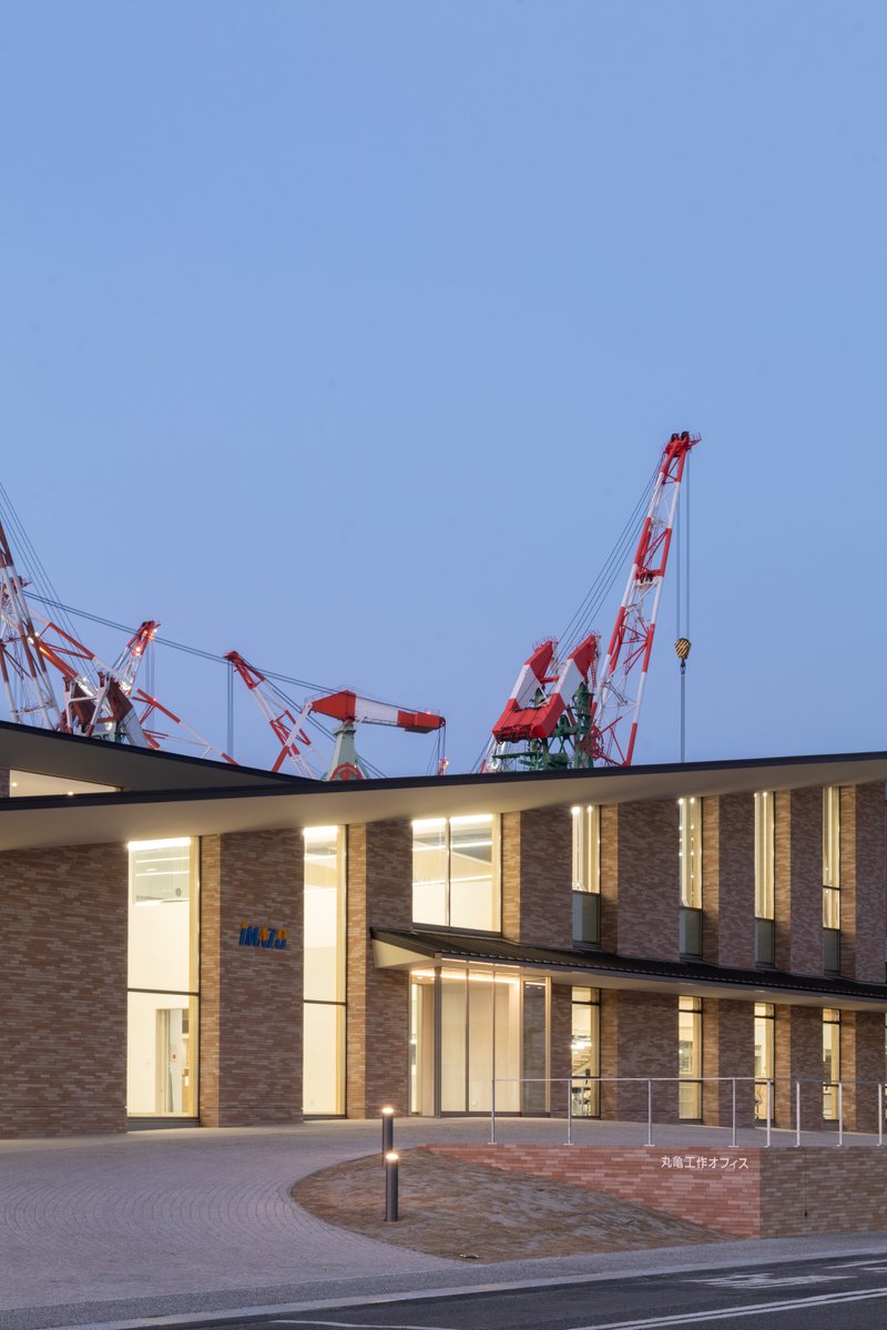 Two-story brick facade with floor-to-ceiling glazing illuminated at dusk beside the curved paved forecourt