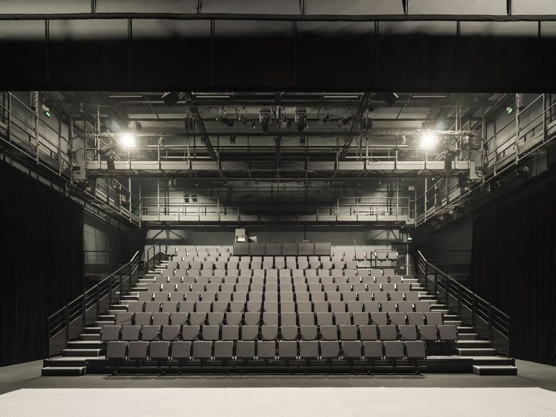 Frontal view of the theatre auditorium with tiered seating and exposed lighting rigging overhead