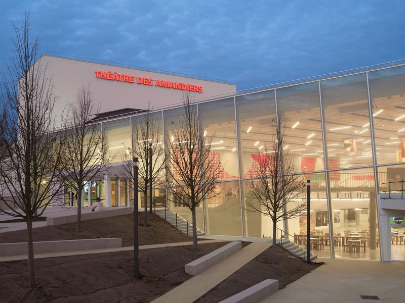 Entrance approach at twilight with bare winter trees and illuminated double-height interior