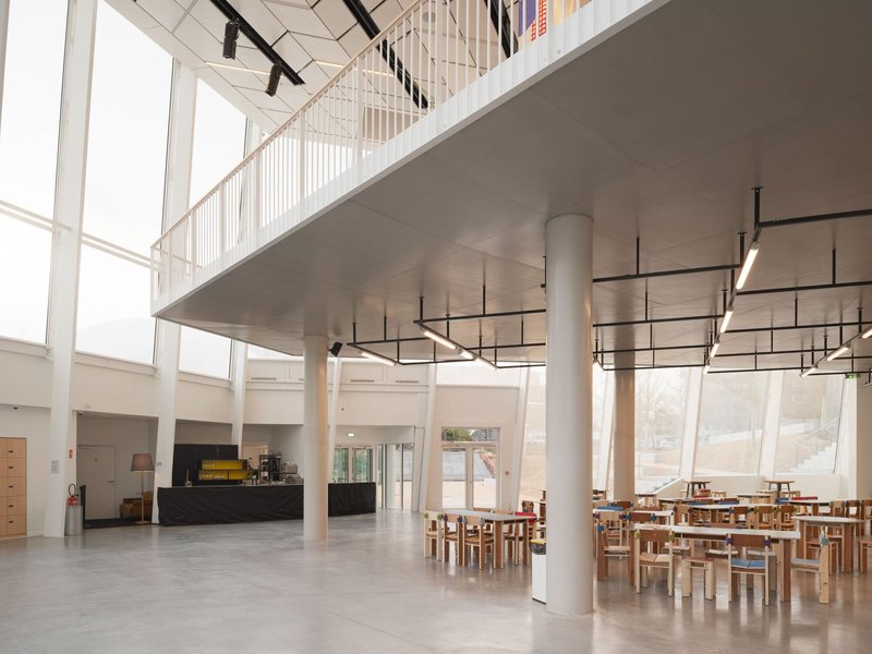 Double-height entry hall with white cylindrical columns, suspended mezzanine, and timber dining furniture