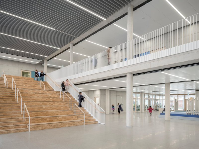 Tiered timber staircase in an atrium with concrete columns and children moving across levels