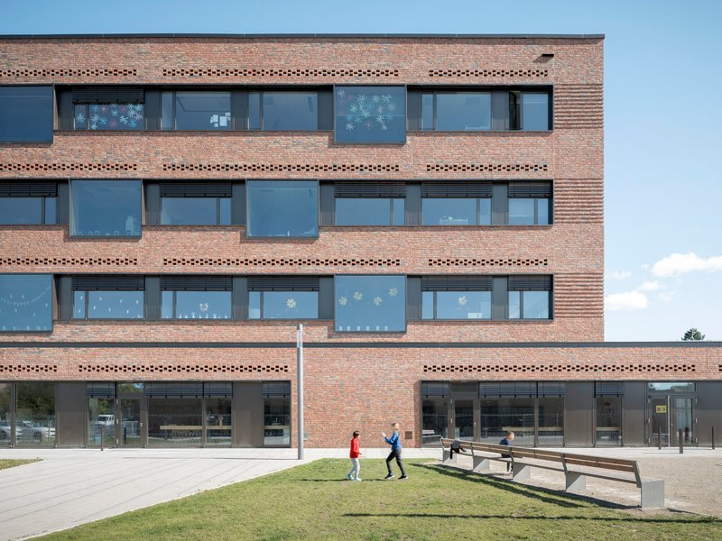 Brick facade with perforated horizontal bands and two figures walking on the lawn below