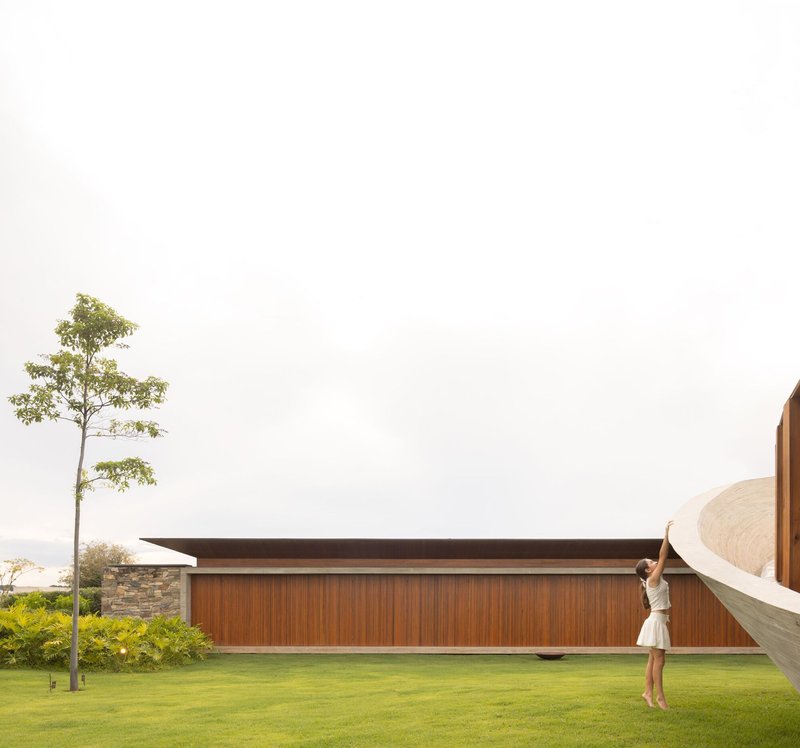 Timber-clad volume with overhanging roof and figure standing near the curved concrete wall on the lawn