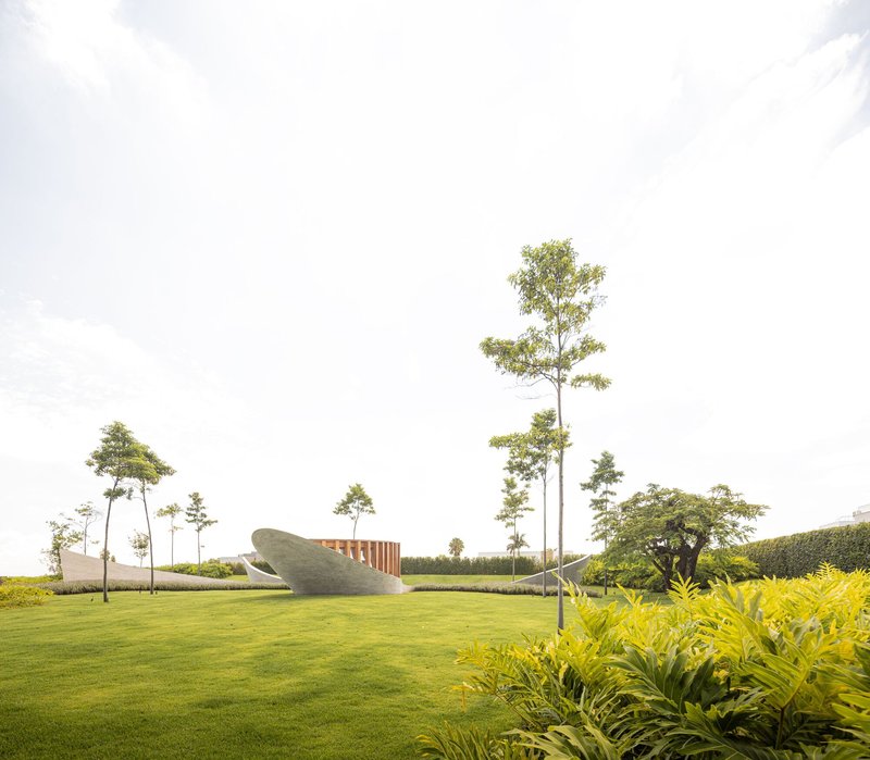Curved concrete volumes with vertical timber fins set in a manicured lawn with young trees and dense planting