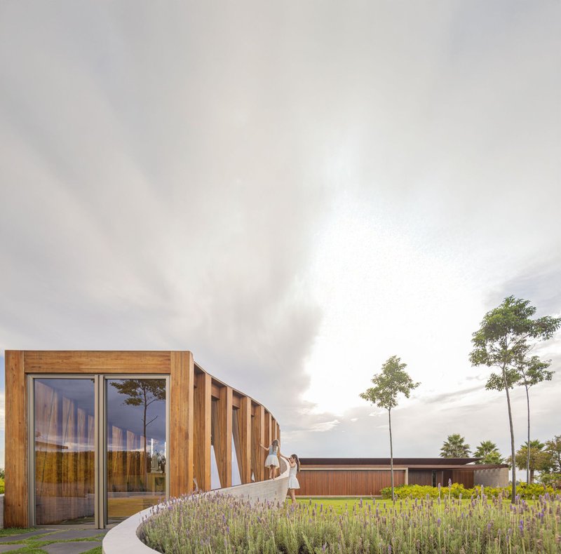 Timber-clad pavilion with vertical slat screen and figure walking through flowering lavender bed at dusk
