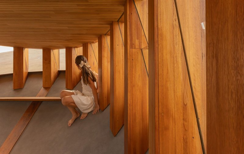 Angled timber wall panels and built-in bench seating with grey concrete floor and seated figure