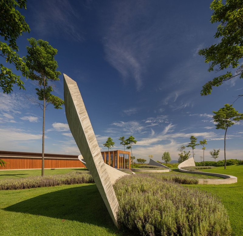 Arcing concrete blade anchoring planted beds and lawn beneath a blue sky with wispy clouds
