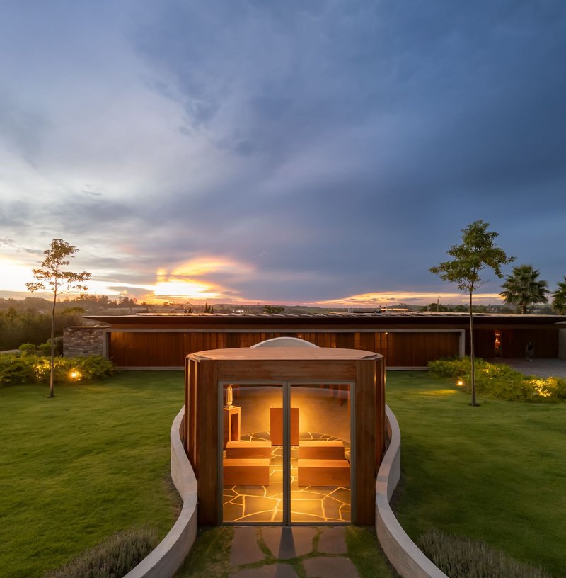 Entry pavilion with illuminated interior and curved white walls flanking a stone pathway at twilight