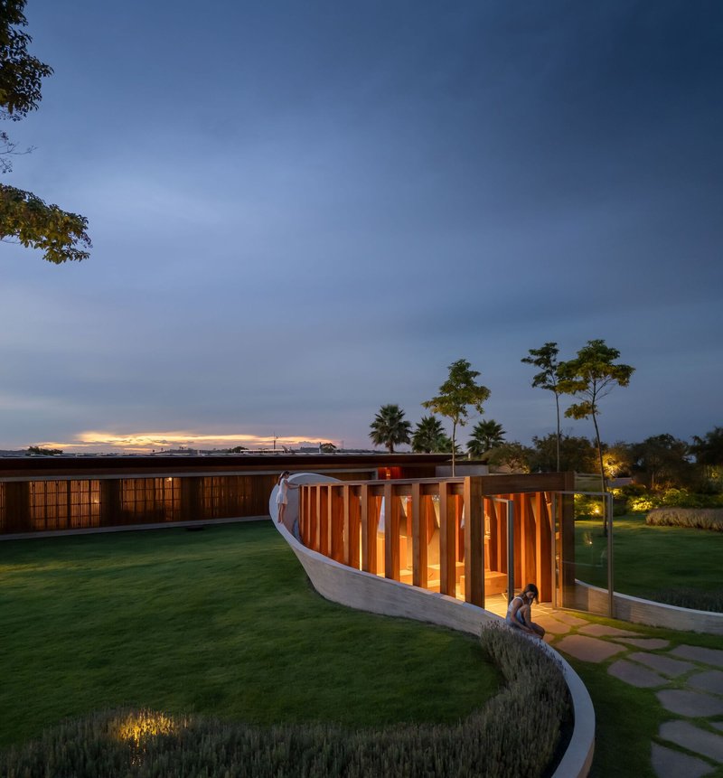 Curved screen wall with illuminated timber slats as two figures walk along the stone path
