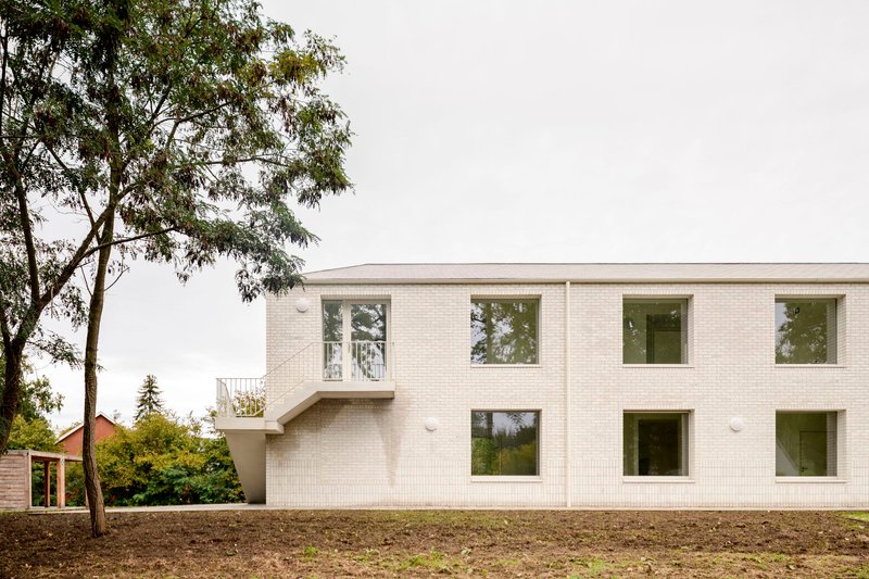 White brick facade with offset windows and cantilevered bay framed by a leafy tree