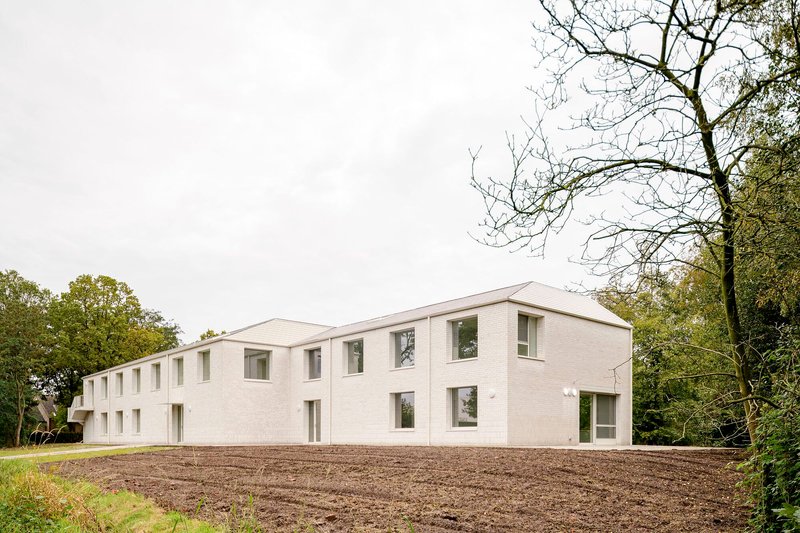 Long white brick facade with gabled roofline on freshly tilled earth beneath bare trees
