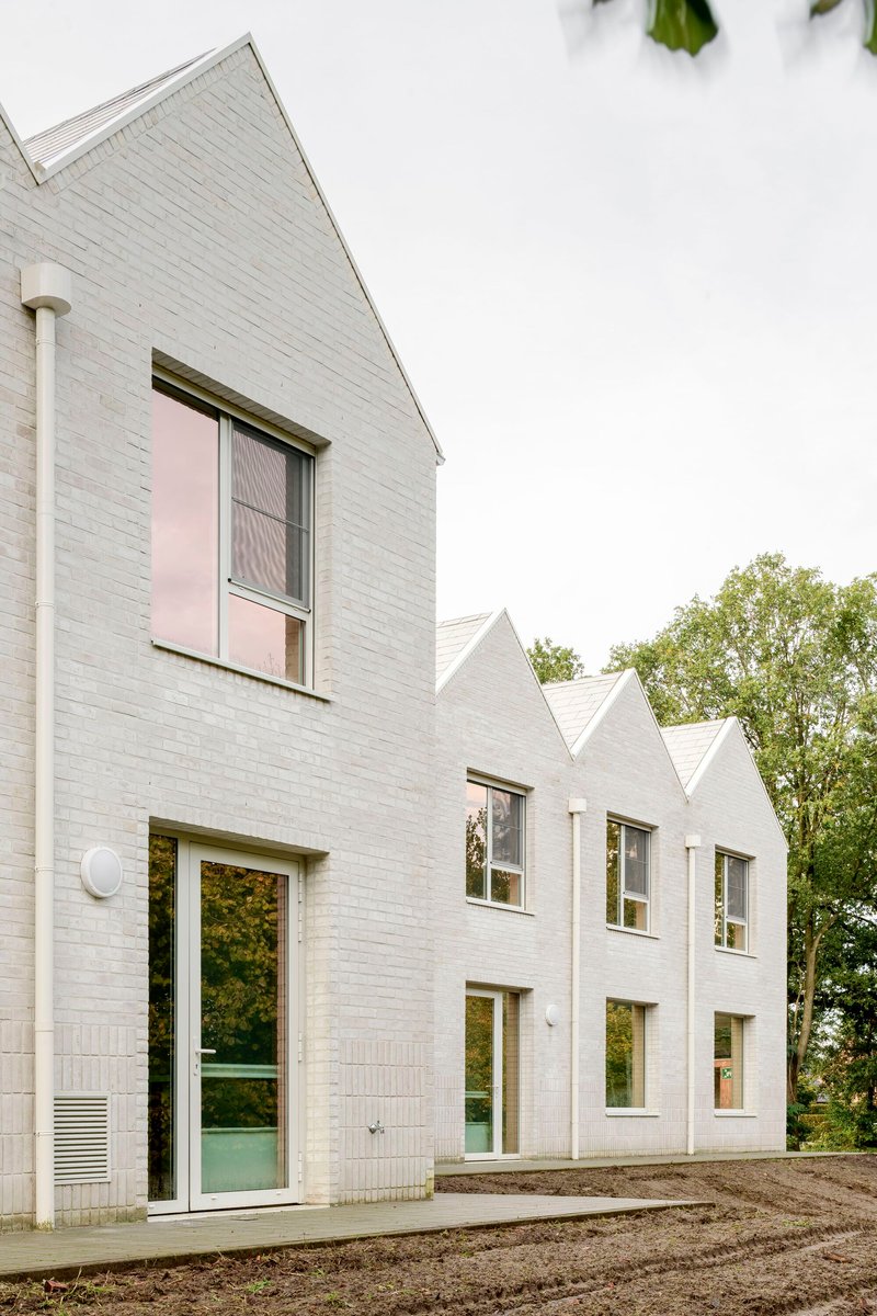 Row of white brick gabled volumes with glazed doors and unpaved earthen foreground