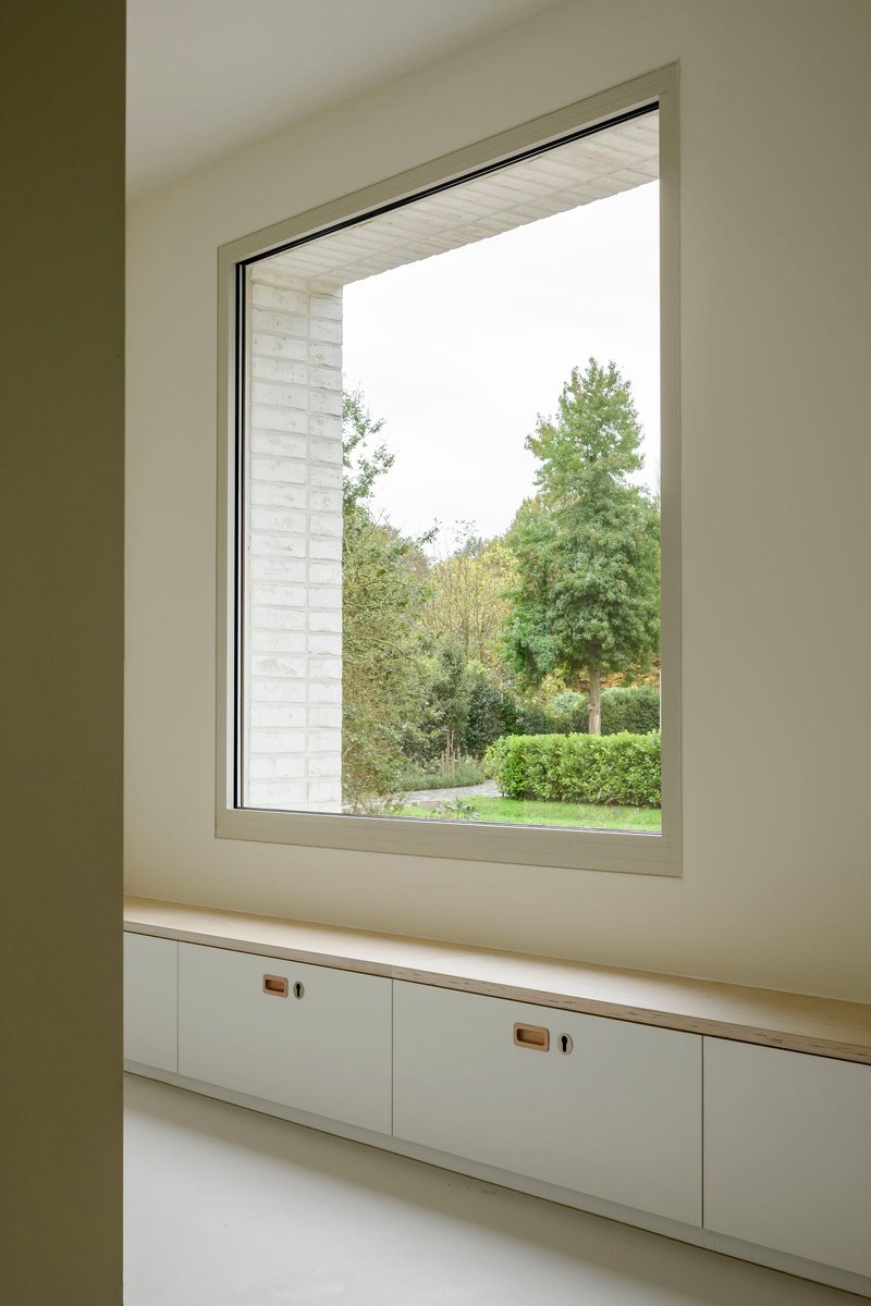 Interior window seat with built-in drawers overlooking green garden through deep brick reveal