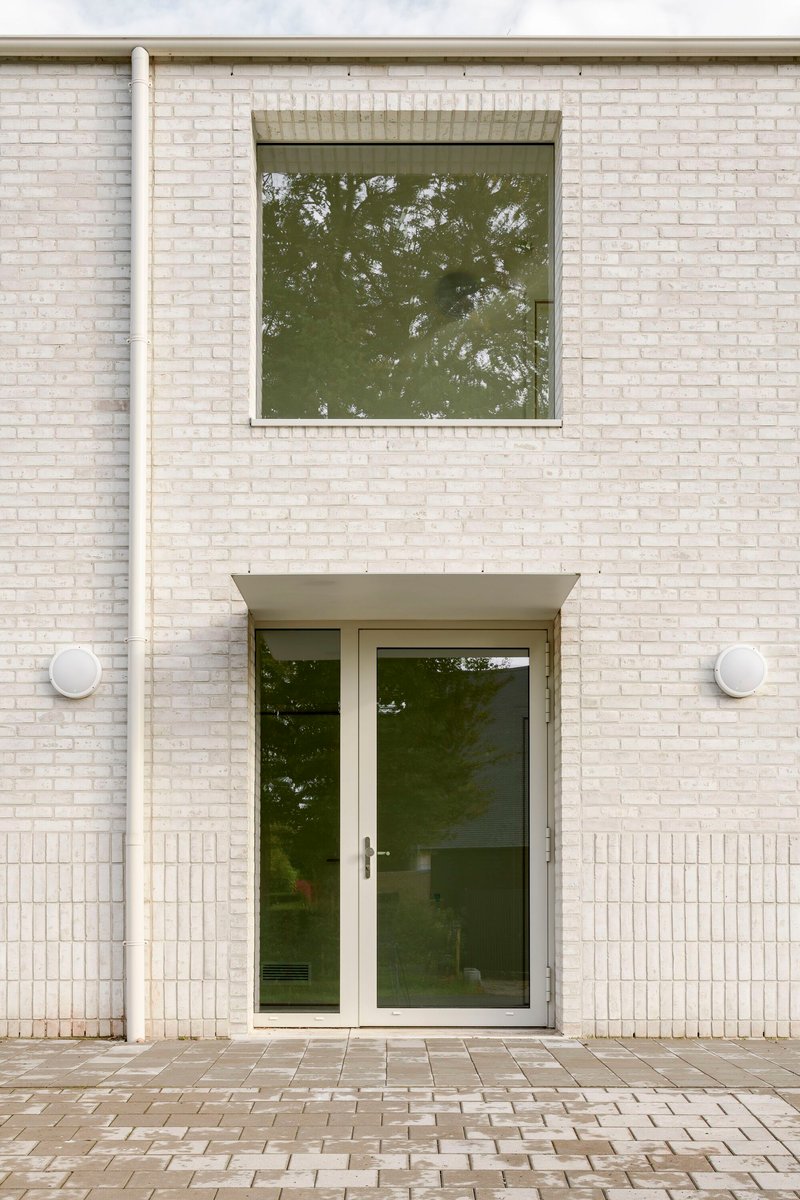Front entry with glass door beneath canopy and square window on white brick facade