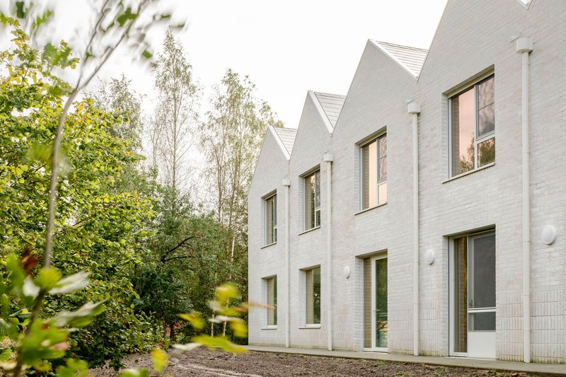 Sawtooth roofline of pale brick housing units framed by birch trees and garden foliage