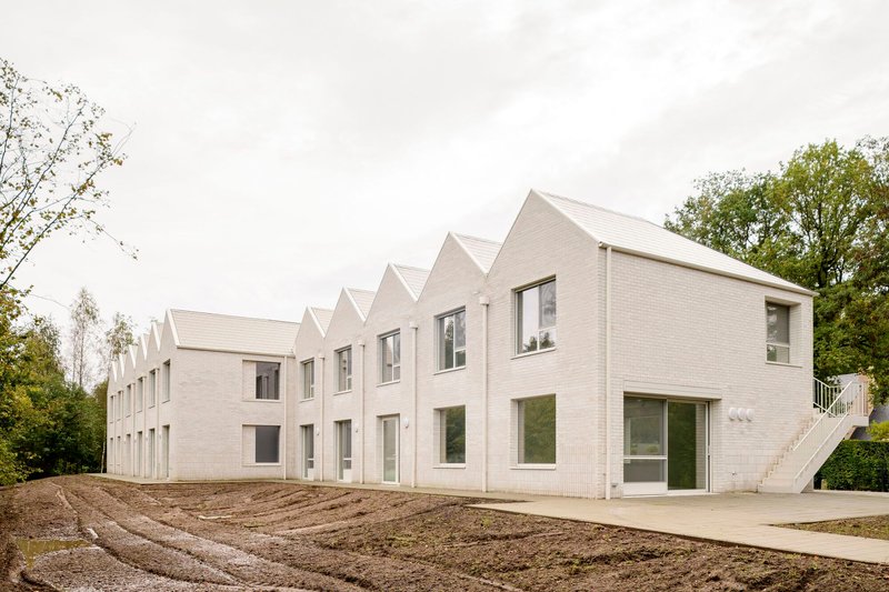 Longitudinal view of repeating gabled volumes in pale brick with freshly graded earth