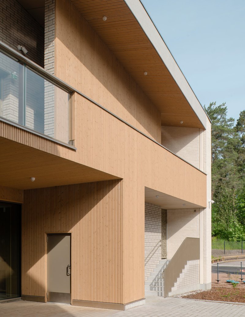 Timber-clad facade with recessed balconies and wood-slatted soffit under a clear sky