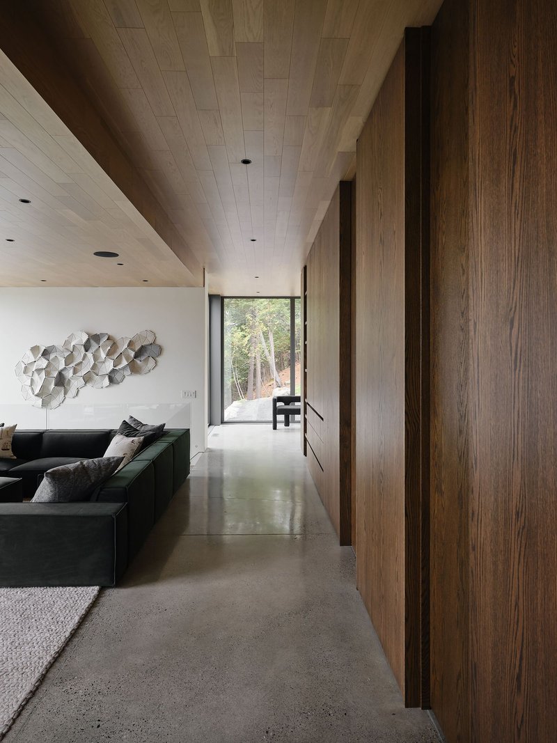 Interior corridor with timber-clad walls and wood plank ceiling leading toward a glazed opening to trees