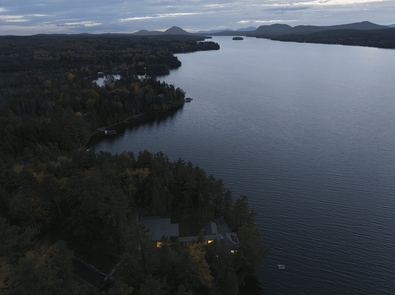 Aerial view of a lakeside residence nestled among dense forest along a curving shoreline at dusk