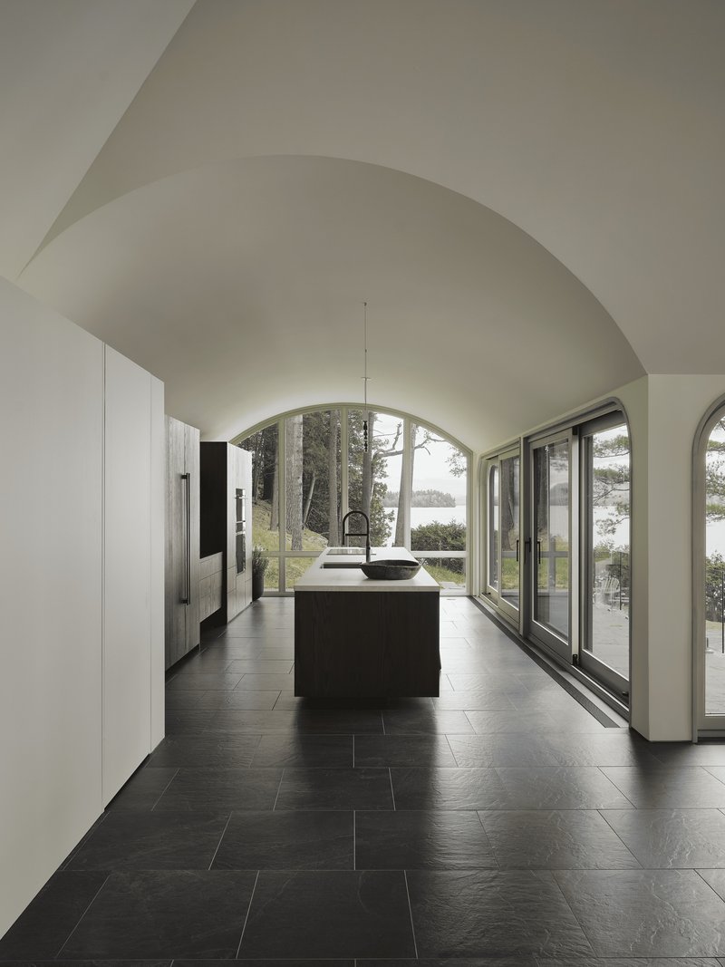 Vaulted kitchen with dark stone floor and arched glazing overlooking the lake
