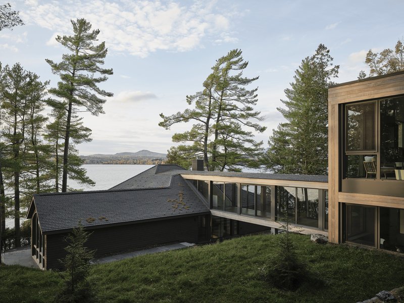 Exterior view showing the dark-shingled volume and timber-framed addition among mature pines