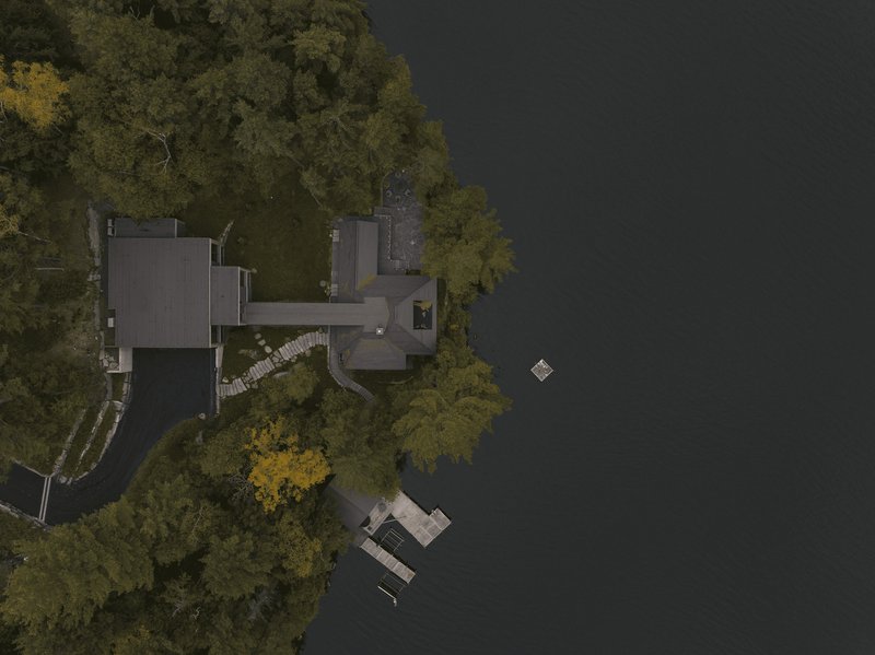 Drone view of the compound on the wooded shoreline with dock in dark water