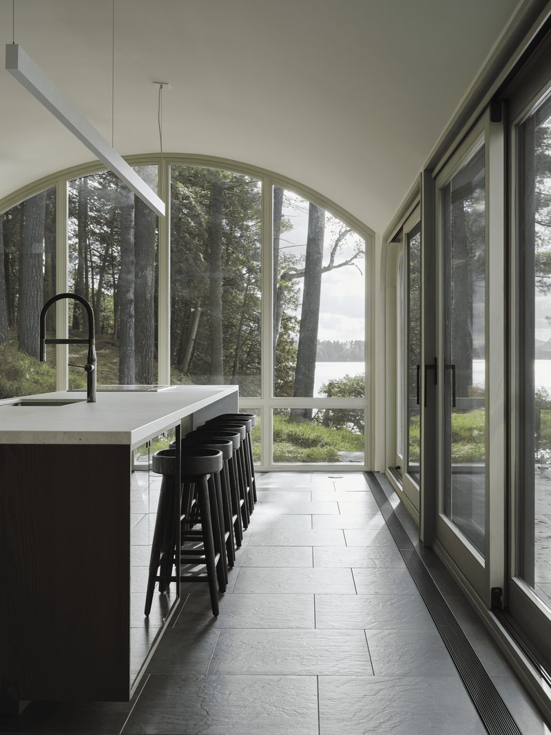Kitchen island with black stools beneath arched windows framing pine trees and water beyond