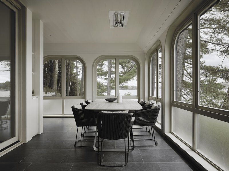 Dining room with arched window bays overlooking the lake through pine forest in overcast light