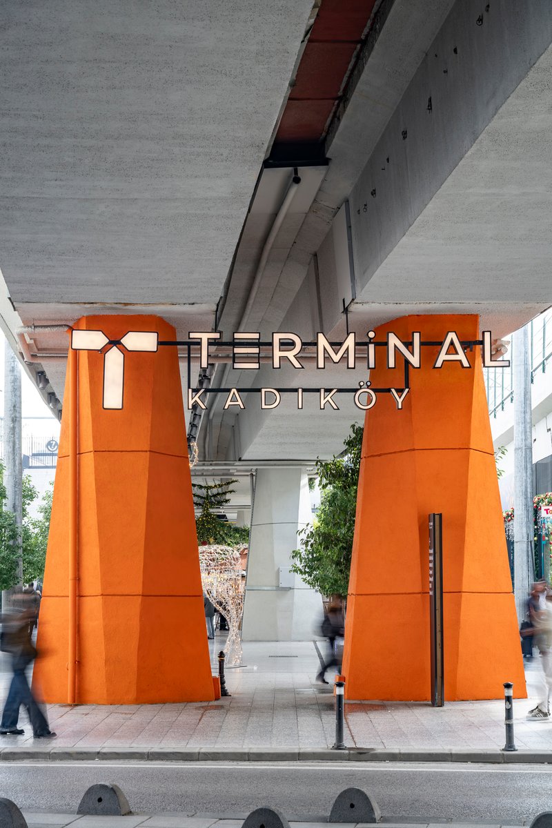 Street-level view of the orange portal columns framing the entrance beneath the elevated roadway
