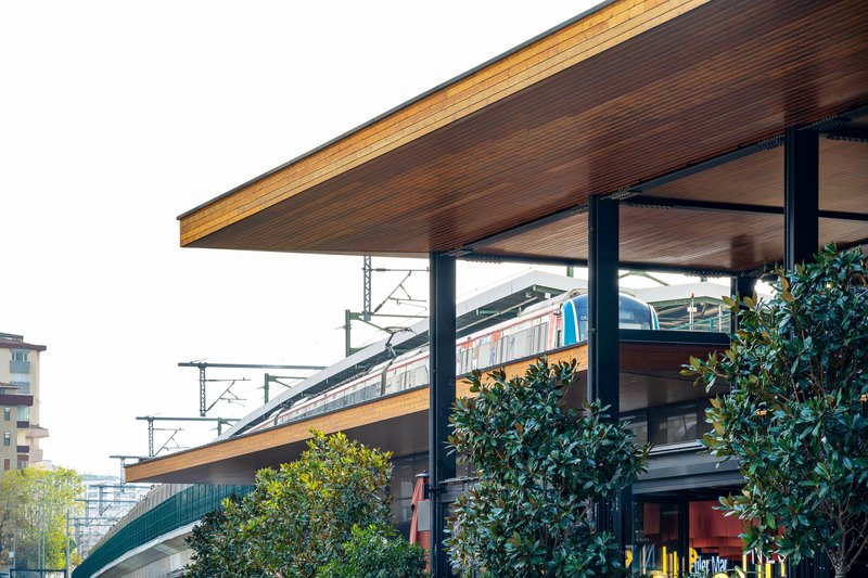 Cantilevered timber soffit roof supported by steel columns above the transit platform with train passing