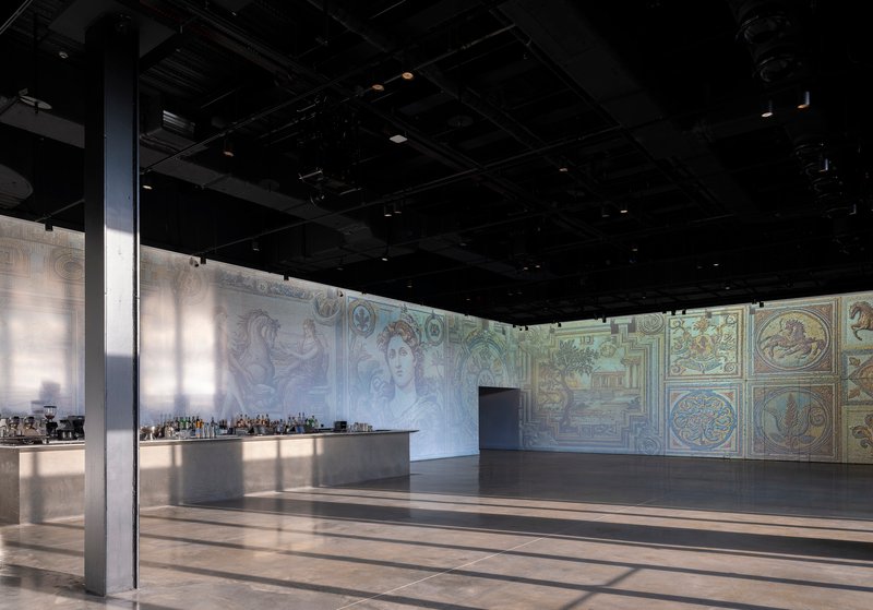 Open event hall with black exposed ceiling, decorative fresco walls, and polished floor reflecting overhead lighting