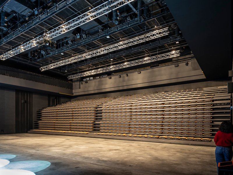 Retractable timber bleacher seating along the wall beneath exposed lighting truss and rigging infrastructure