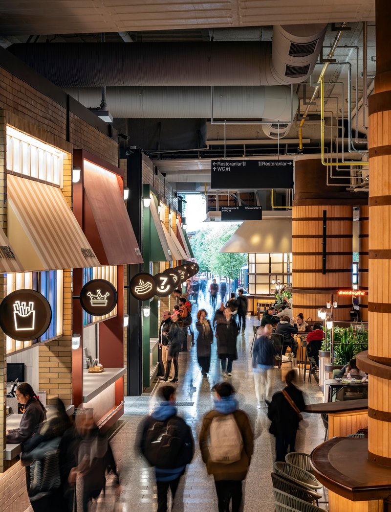 Interior passage with tiled food kiosks under exposed ductwork as pedestrians move through the corridor