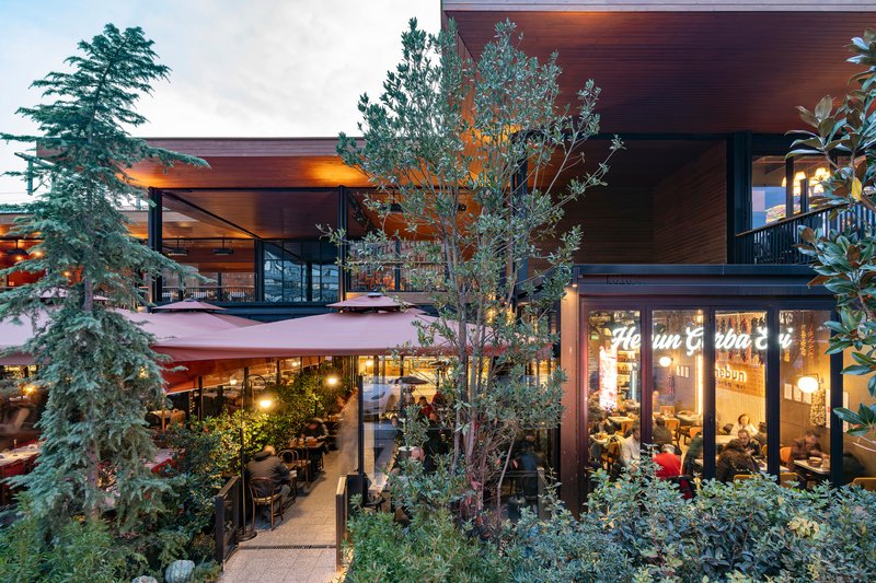 Two-level timber-clad structure with planted terraces and glass-enclosed dining areas at dusk