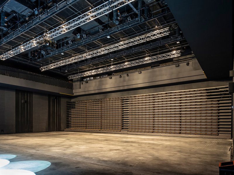 Horizontal wooden slat wall system in partially closed position beneath theatrical lighting grid