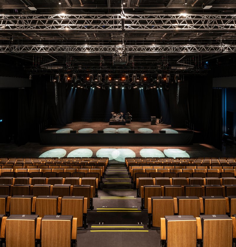 View from auditorium toward stage with timber seats, circular stage platforms and theatrical lighting above