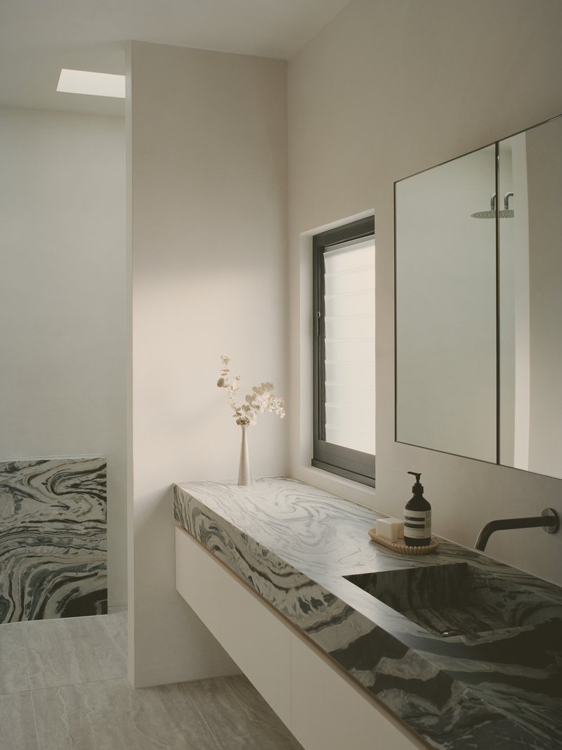 Bathroom vanity with swirled grey marble countertop and integrated basin under soft skylight illumination