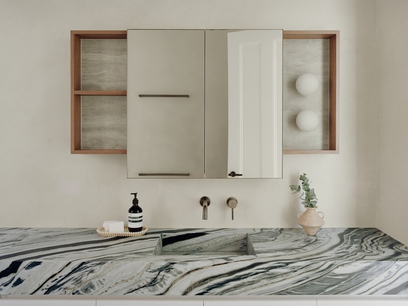 Marble vanity with integrated sink below timber-framed mirror cabinet and wall-mounted brass fixtures
