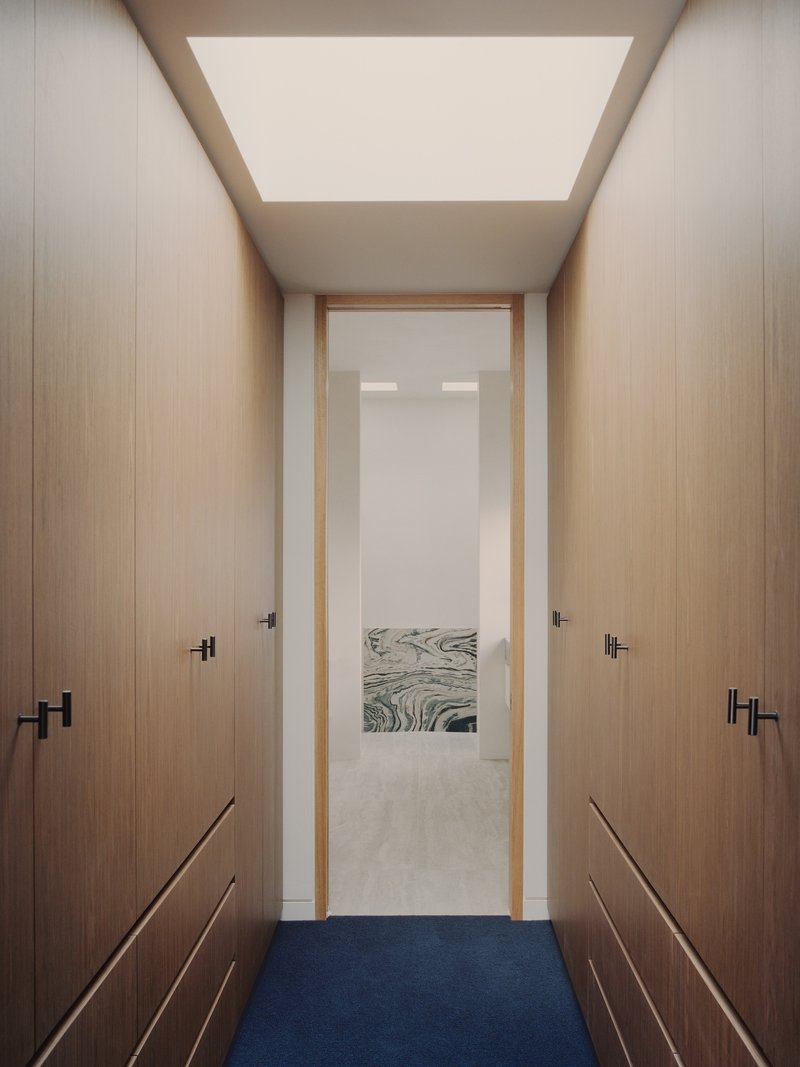 Narrow dressing corridor with timber wardrobes flanking a doorway framed by large ceiling skylight