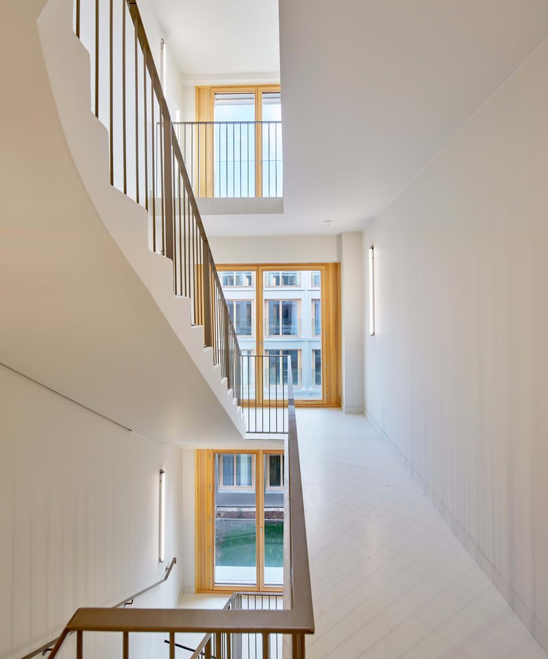 Multi-story stairwell with timber handrails and white walls illuminated by timber-framed windows at each landing