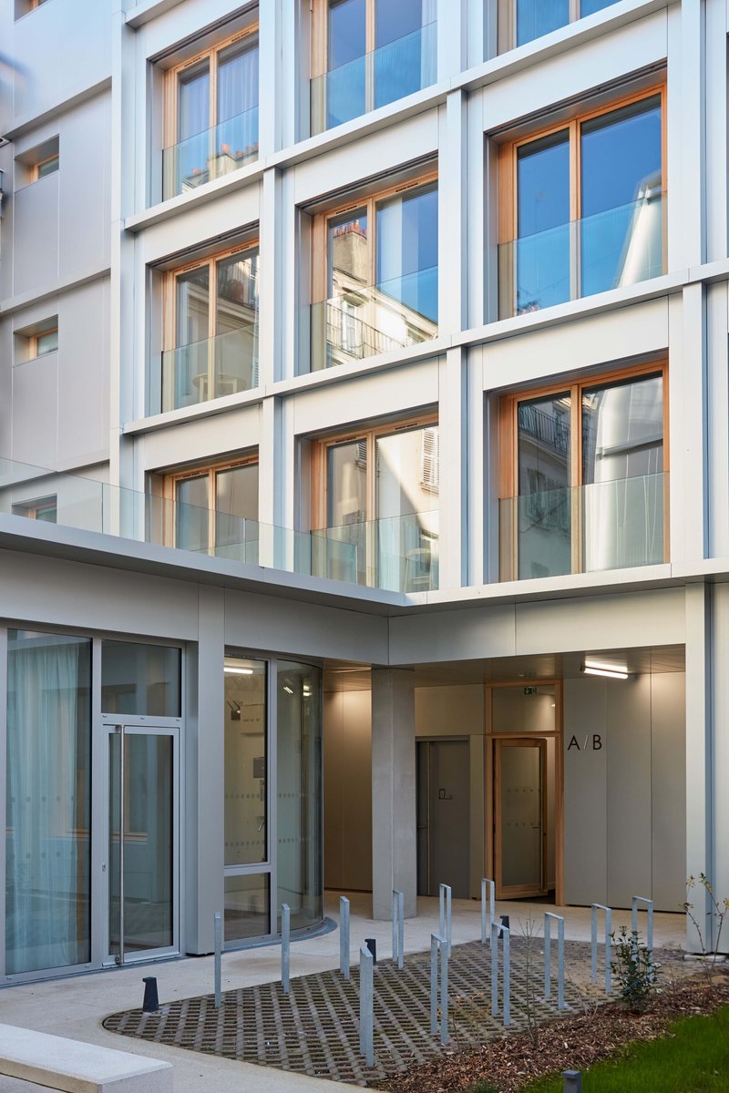 Courtyard view showing white facade with timber-framed windows and landscaped planters with young trees